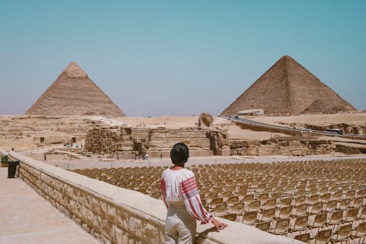 A tourist admires the Great Pyramids and Sphinx in Giza, Egypt under the clear daytime sky.