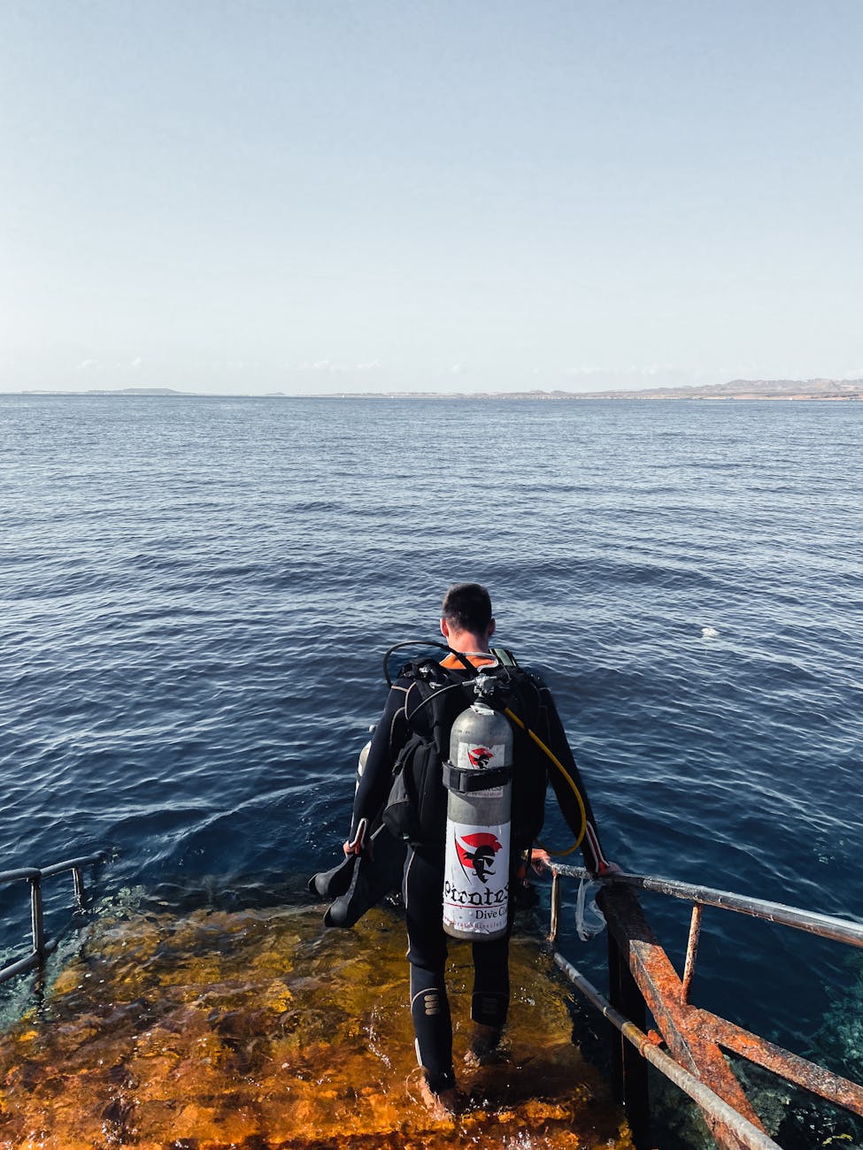 A scuba diver in a drysuit embarking on a diving adventure from a step in Sharm El-Sheikh, Egypt.