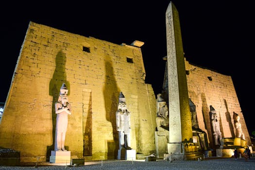 Night view of illuminated ancient statues and obelisk at Luxor Temple, Egypt.