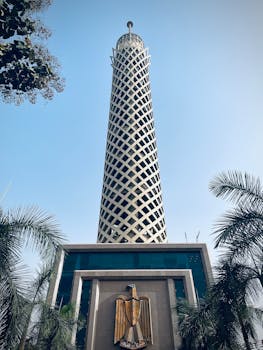 Striking view of the Cairo Tower, a prominent Egyptian landmark, set under a clear blue sky with surrounding palm trees.