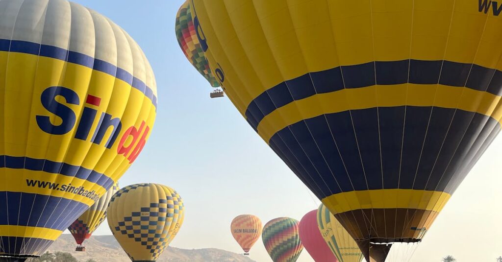 Colorful hot air balloons soar over Luxor, Egypt with tourists preparing for flight.