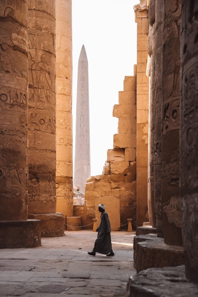 A serene view of the Karnak Temple's ancient columns and obelisk with a person walking through.