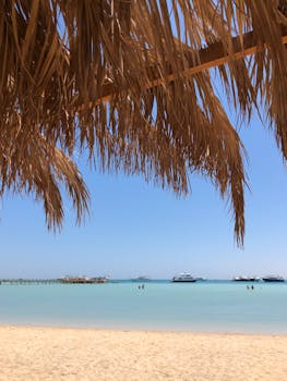 Relaxing beach view in Hurghada, Egypt with clear blue water, boats, and palm leaves.