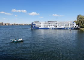 A ferry boat and rowboat on the Nile River under a clear blue sky in Luxor, Egypt.