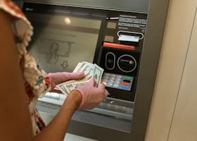 A person wearing gloves withdraws cash from an ATM, ensuring hygiene.