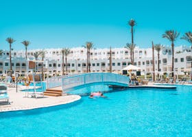 Scenic view of a resort pool with a footbridge and palm trees under a clear sky.