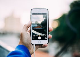 Close-up of a hand holding a smartphone while capturing a cityscape outdoors.